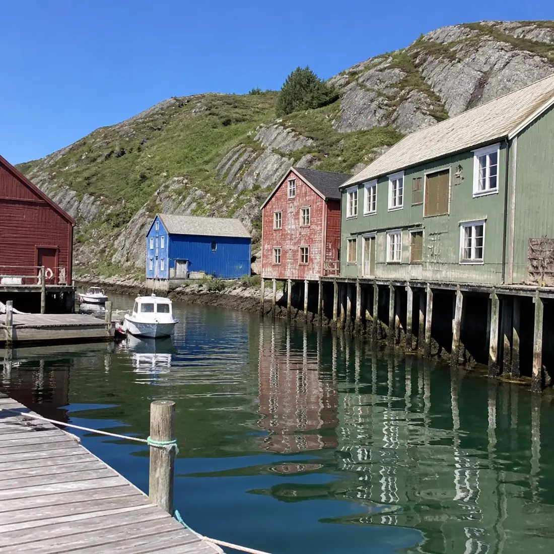 KI-generert testbilde av en gammel norsk fiskehavn med slitte sjøhus på påler i falmet rødt, blått og grønt